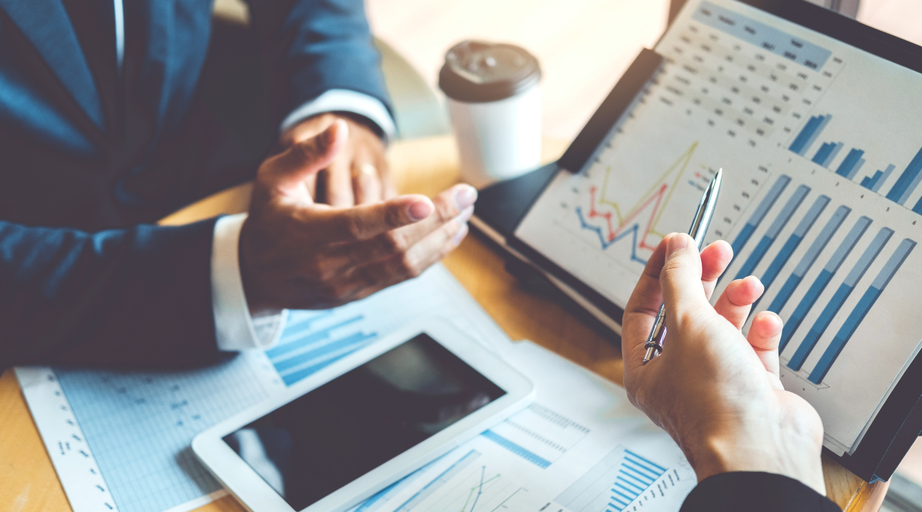 Hands gesturing towards financial documents and screens with graphs and charts