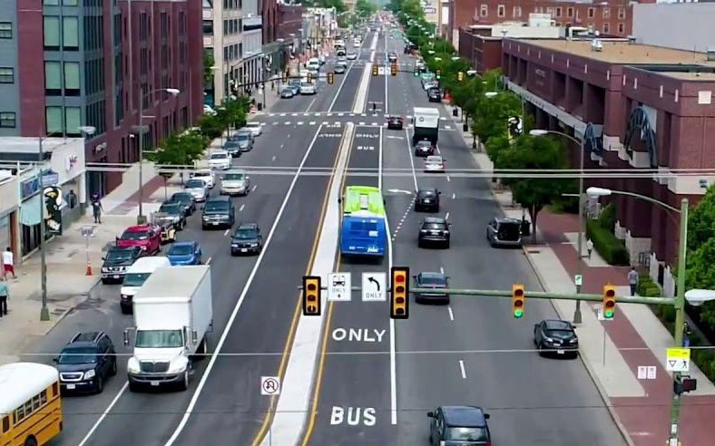 This image shows an aerial view of a pulse bus riding in a bus only lane down the middle of broad street lined by brick VCU buildings