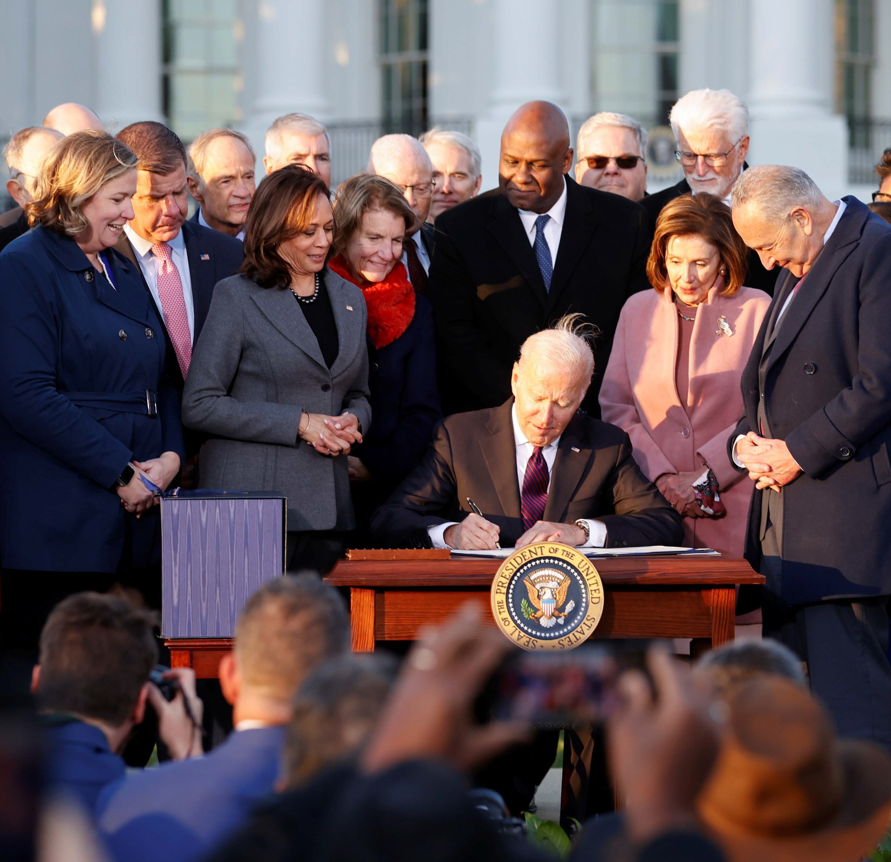 This image shows President Biden signing a bill surrounded by lawmakers and the Vice President. 