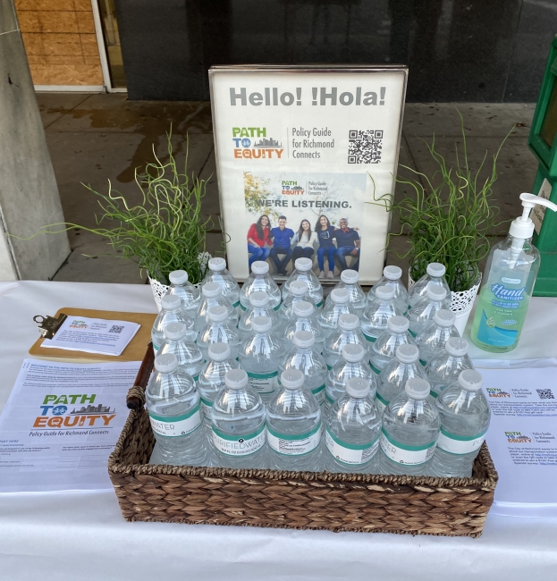 A table with a sign containing information about the online survey, with bottles of water and hand sanitizer. 