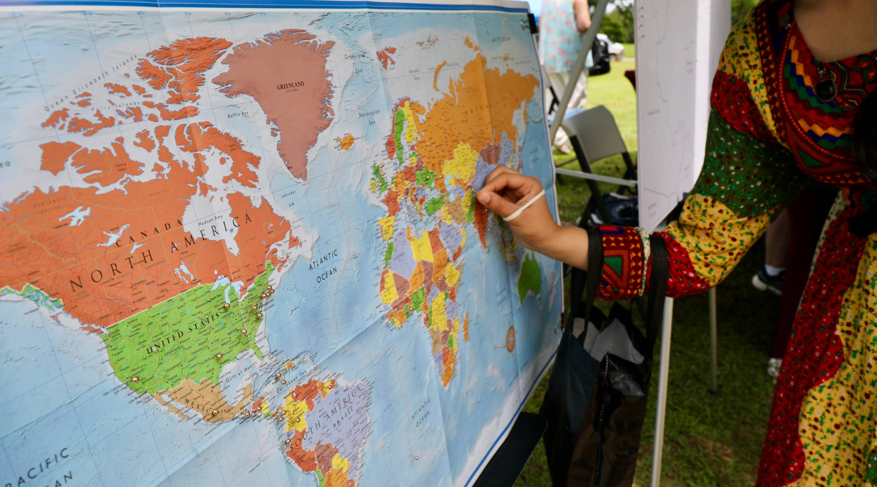 A person in a colorful dress writes on a map of the world. 