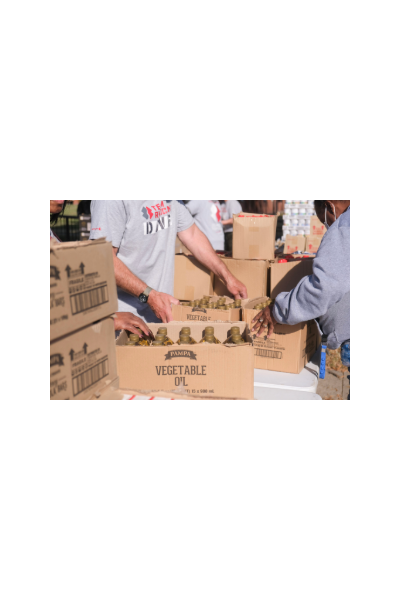 hands load a box of vegetable oil for a donation event at a local community center.
