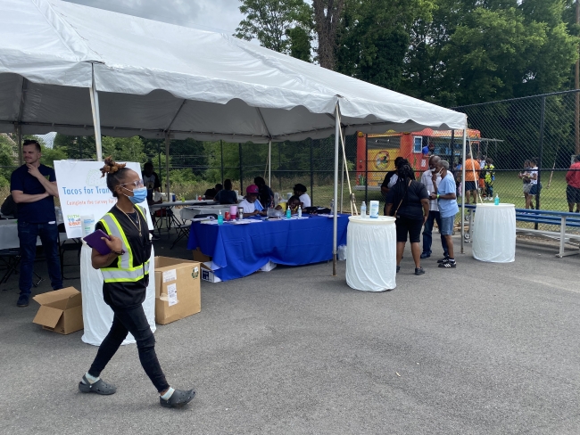 This image contains a large white outdoor party tent with a person in a yellow vest holding a clip board ready to take surveys.