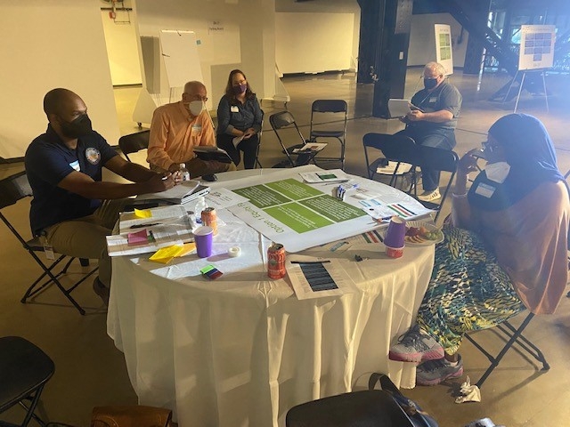 A group of people sit around a round table with large format papers in front of them.